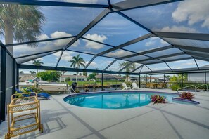 Une piscine extérieure couverte offrant une vue sur des palmiers et des maisons en arrière-plan.
