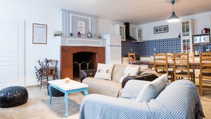 Una sala de estar acogedora con chimenea, un comedor con sillas de madera y una cocina con salpicadero de diseño azul.