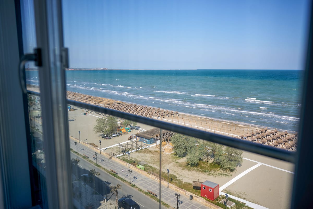 A view of a beach from a window, including the sea, beach umbrellas, and a parking area.
