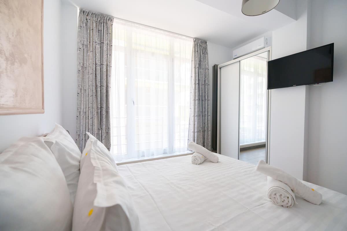 A hotel room with a bed, curtains, a flat-screen TV, and a window.