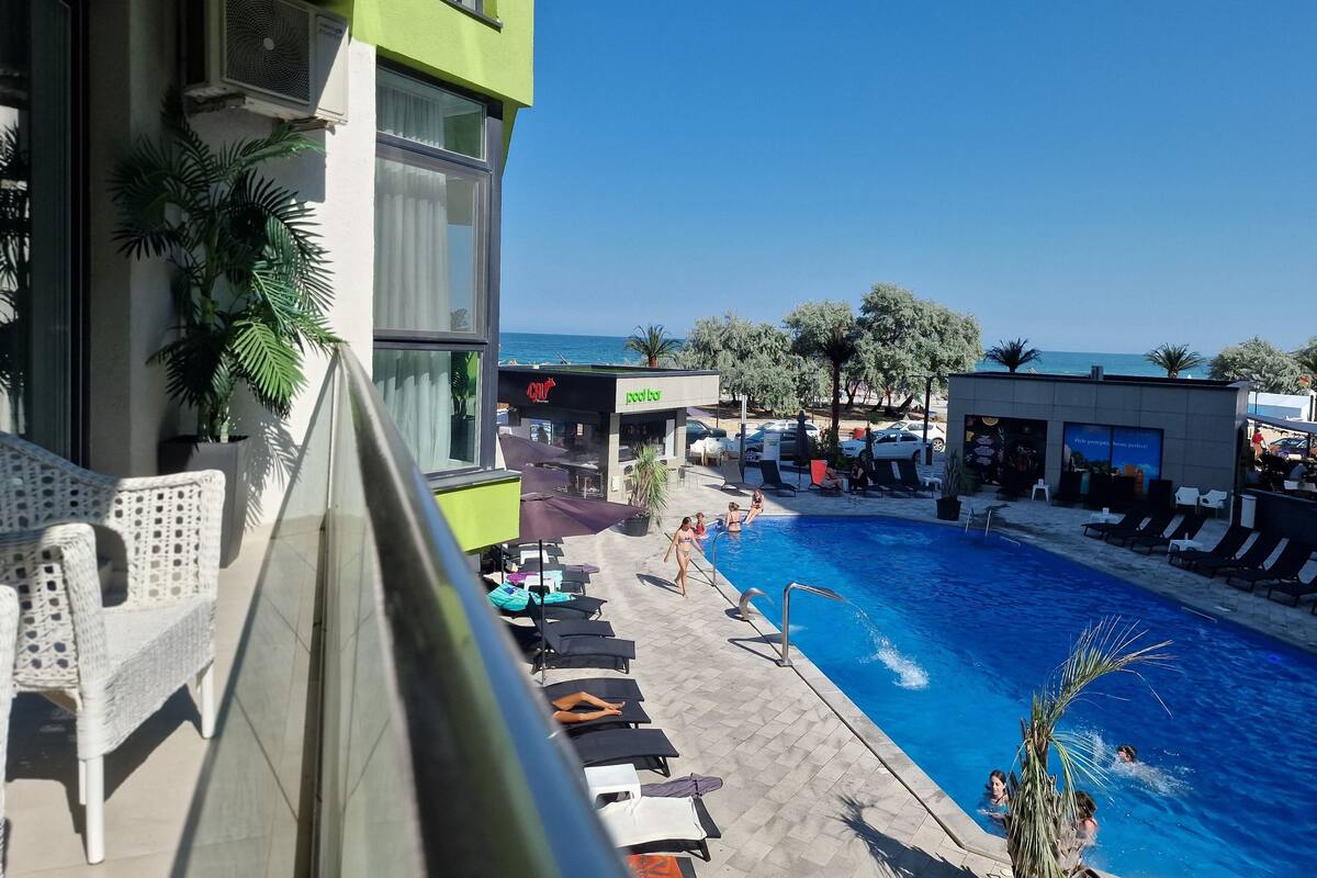 A pool area with lounge chairs and umbrellas, a clear view of the sea, and a building with a 'pool bar' sign.