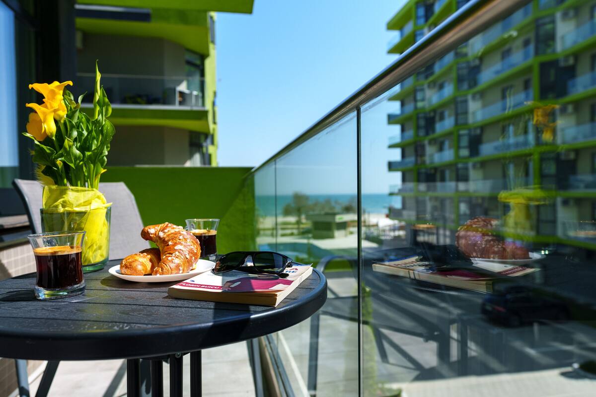 A balcony with a table set for breakfast, including croissants, a drink, and a book.