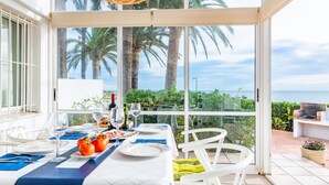A dining area with a table set for two, a view of the sea, and palm trees outside.