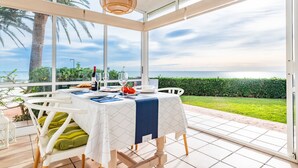 A dining area with a table set for two, overlooking a scenic view of the sea and greenery.