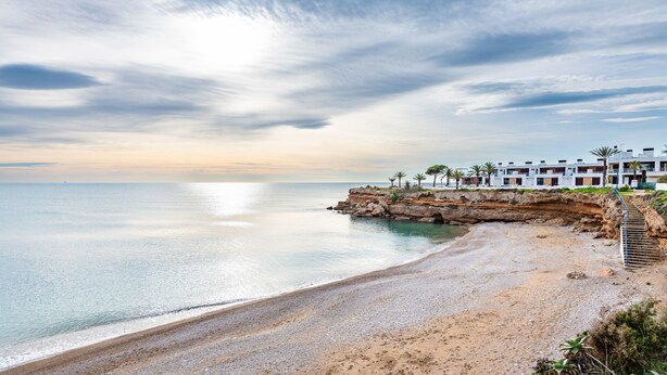 A coastal hotel with a beach view, a rocky cliff, and a clear sky.