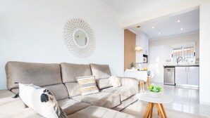 A modern living room with a beige sectional sofa, a round mirror, and a small round table with a plant.