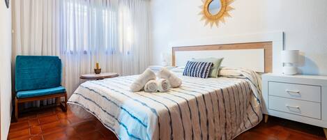 Habitación de hotel con cama, una silla, una mesita de noche y un espejo con forma de sol en la pared.