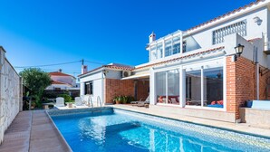 A swimming pool with a tiled edge, a patio area with chairs, and a building with a tiled roof and brick walls. - Villa Monbijou with Private Pool & Wi-Fi close to the Beach (Vinarós)