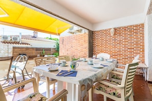 An outdoor dining area with a brick wall, a yellow umbrella, and a table set with plates, cups, and a fork.