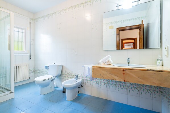 A bathroom with a toilet, bidet, and sink, a mirror above the sink, and a window.
