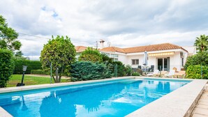 Una piscina con bordo piastrellato, circondata da una recinzione, e una casa con tetto in tegole sullo sfondo.
