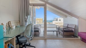Une pièce dotée d’une porte vitrée donnant sur un balcon, d’un bureau avec une chaise et d’un canapé.