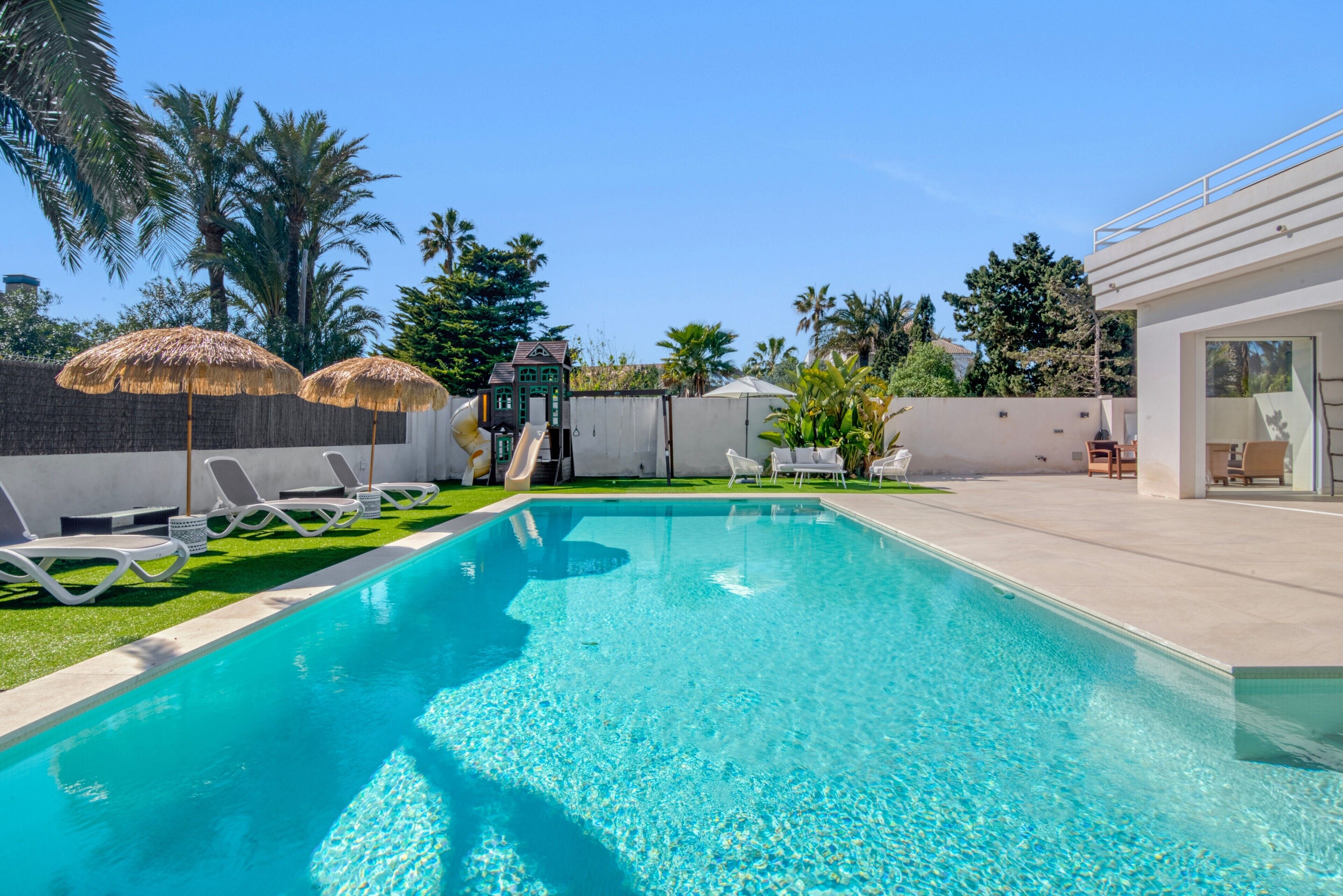 A swimming pool with lounge chairs, a slide, and palm trees.