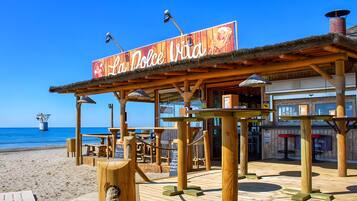 Ein hölzernes Café am Strand, mit einem Schild mit der Aufschrift 'La Dolce Vita' und Blick aufs Meer.