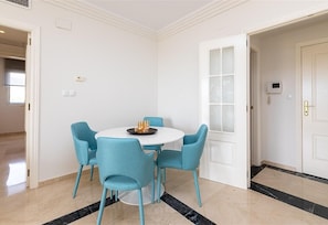 A room with a round table, four chairs, a door with frosted glass panels, and a white wall with a light switch.