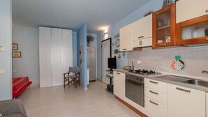 A compact kitchen with white cabinets, a built-in oven, and a dining area with a red sofa. - Studio Residence Valle Fiorita with Shared Pool & Wi-Fi in Riotorto (Piombino)