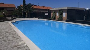 A swimming pool with a tiled deck, surrounded by buildings with red-tiled roofs and palm trees. - Studio Residence Valle Fiorita with Shared Pool & Wi-Fi in Riotorto (Piombino)