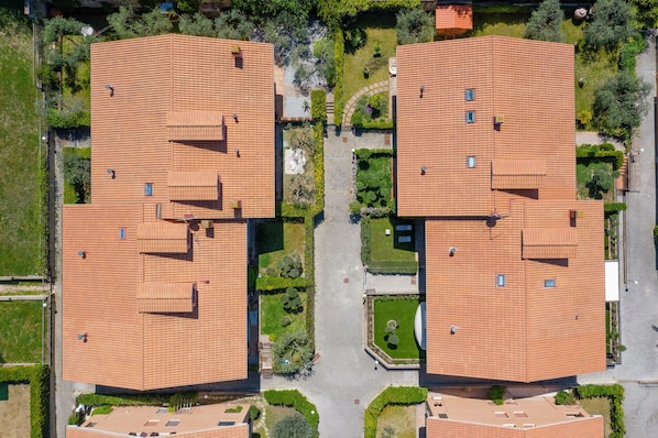 An aerial view of a residential area with two buildings featuring red-tiled roofs, surrounded by green spaces and pathways.