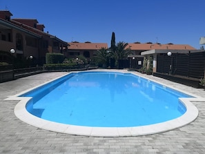 A rectangular swimming pool with a tiled edge, surrounded by a brick patio.