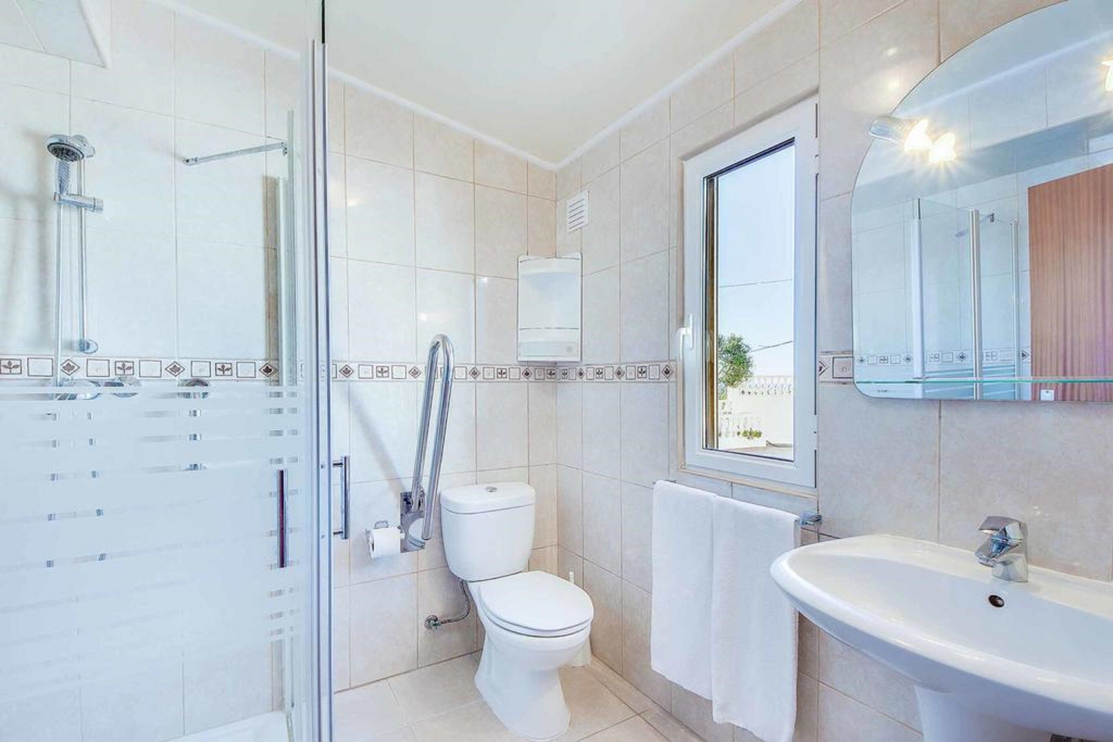 Un baño moderno con cabina de ducha de vidrio, inodoro, lavamanos y ventana con vistas.