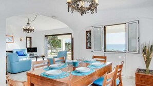 A dining area with a wooden table set for four, blue cushions, and a chandelier. - Villa Brigida with Sea View, Heated Pool & Wi-Fi (São Rafael)