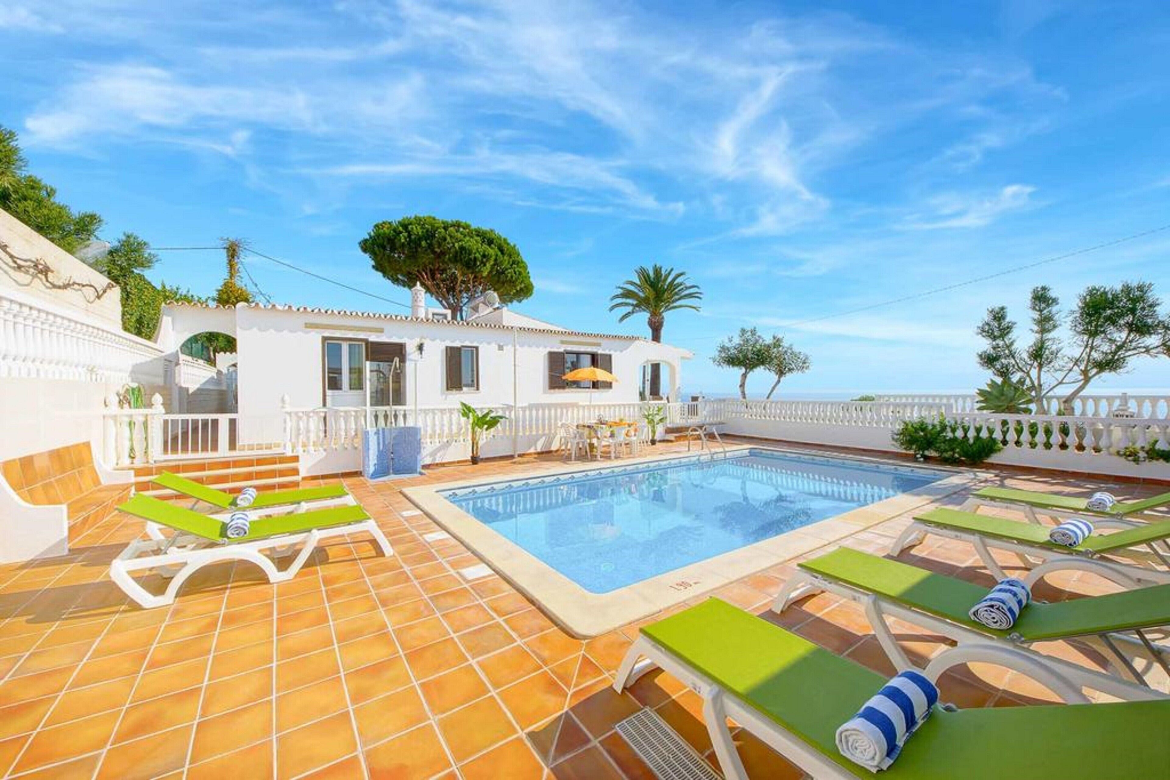 Ein Swimmingpool mit Liegestühlen, ein weißes Gebäude und ein klarer Himmel.