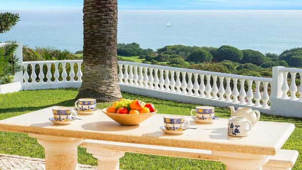 A table with a fruit bowl and tea set, a white fence, and a view of the sea. - Villa Brigida with Sea View, Heated Pool & Wi-Fi (São Rafael)