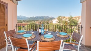 A wooden table set for four with blue plates, surrounded by white chairs, on a balcony with a mountain view. - "Elegante appartamento centro" with 2 Terraces & Wi-Fi (san teodoro)