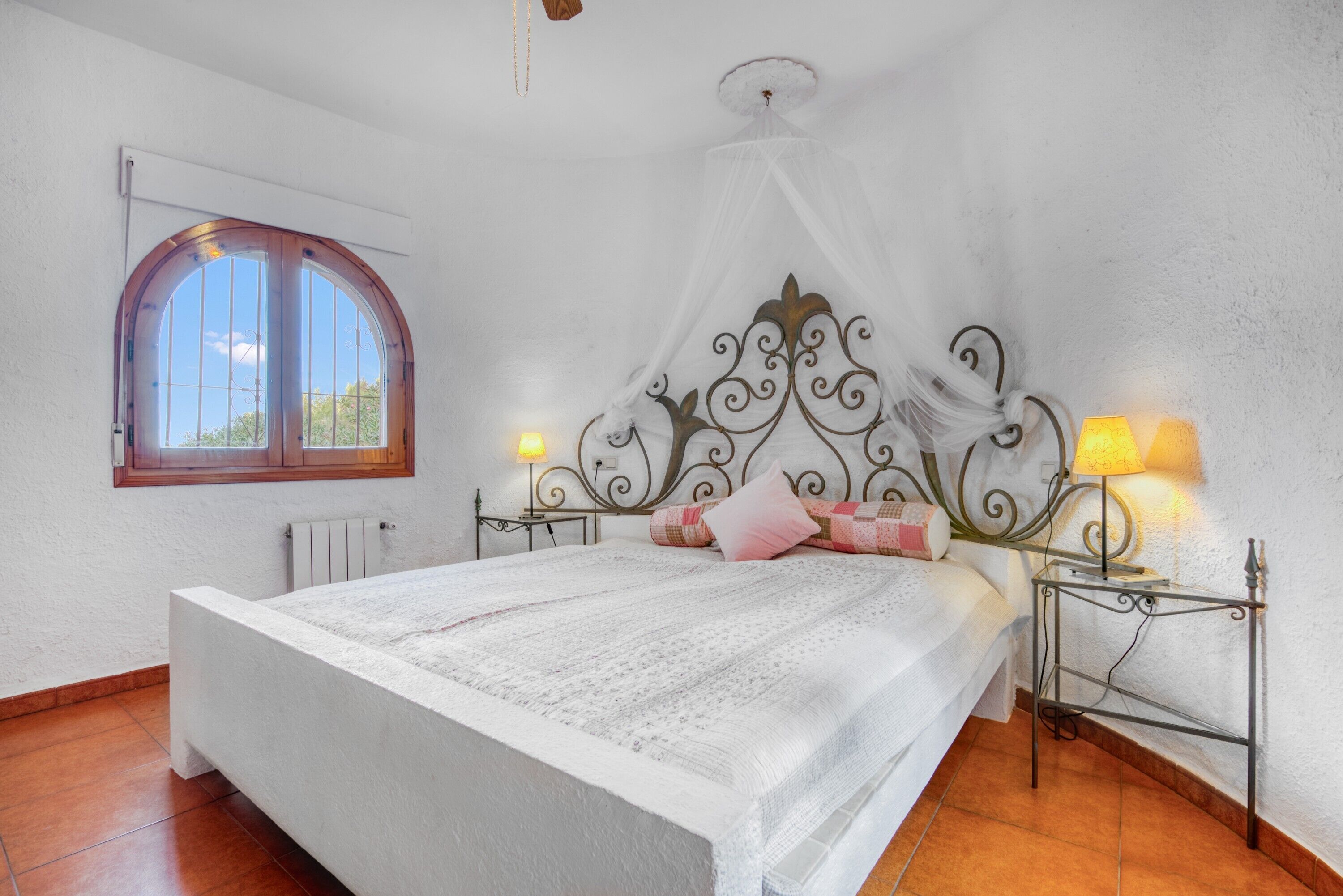A bedroom with a large bed, a window, a decorative headboard, and bedside lamps.