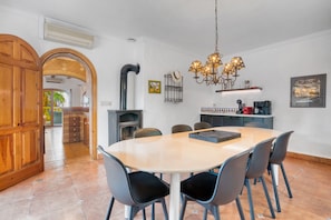 Un comedor con una mesa redonda, sillas, una araña y una cocina al fondo.