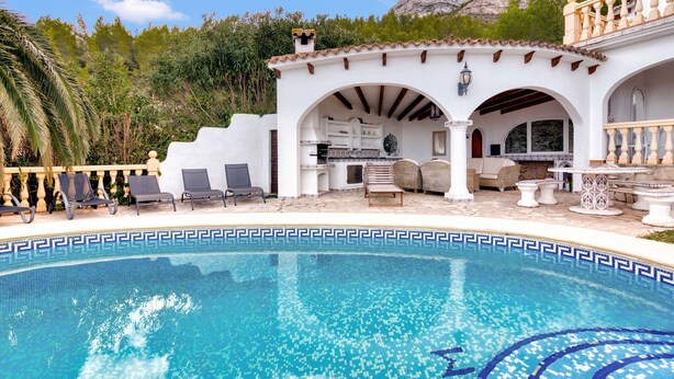 Un espace aménagé au bord de la piscine, avec un bâtiment blanc, des sièges en plein air et une chaîne de montagnes en arrière-plan.