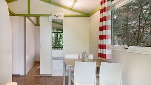Ein Essbereich mit Tisch und Stühlen, ein Fenster mit Blick auf Bäume und eine Tür zu einem weiteren Raum.