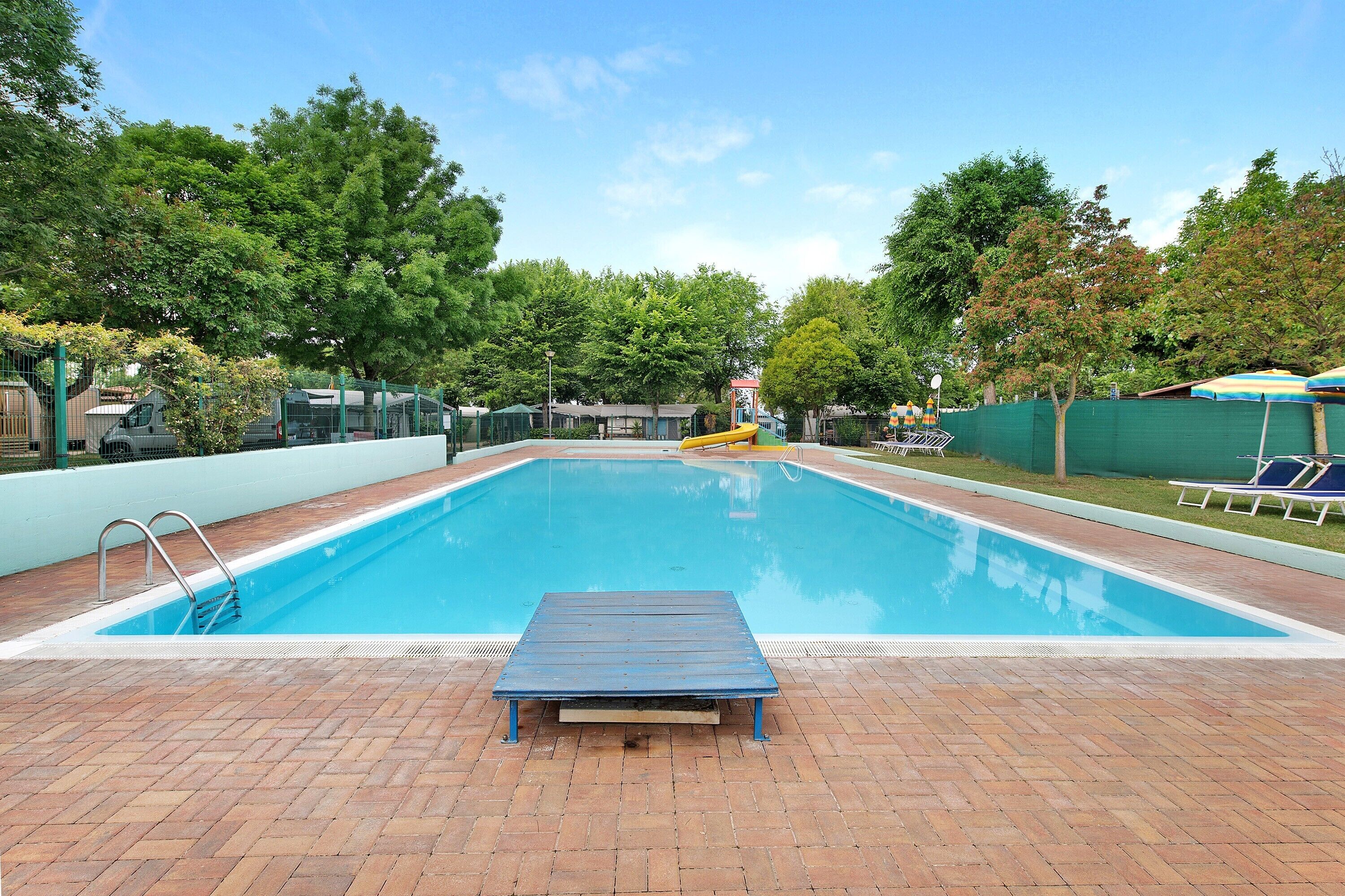 A swimming pool with a wooden deck, a slide, and lounge chairs.