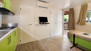 Une cuisine compacte équipée d’une cuisinière à gaz, de meubles blancs et verts, d’un téléviseur encastré et d’une fenêtre avec des rideaux.