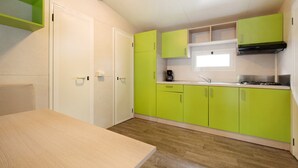 Une cuisine de taille réduite avec des meubles de couleur verte, un plan de travail en bois et une fenêtre située au-dessus de l’évier.
