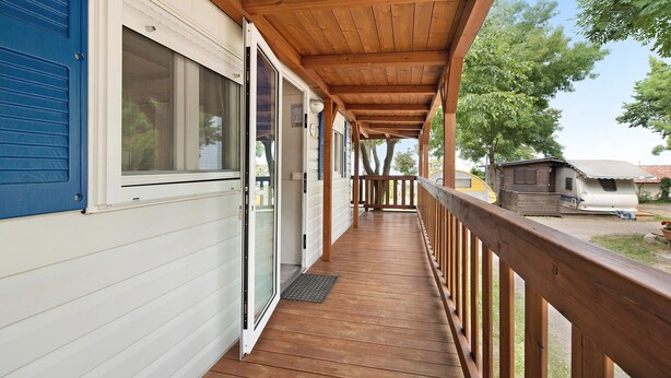 Une véranda couverte avec des balustrades en bois, une porte-fenêtre coulissante et, au loin, une vue sur un terrain de camping.