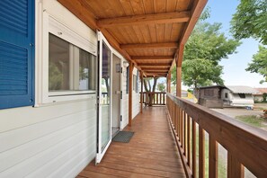 A covered porch with wooden railings, a sliding glass door, and a view of a campsite in the background. - Apartment "Casa Mobile 16 Amici di Lazise" with Lake View, Pool & A/C (Lazise)