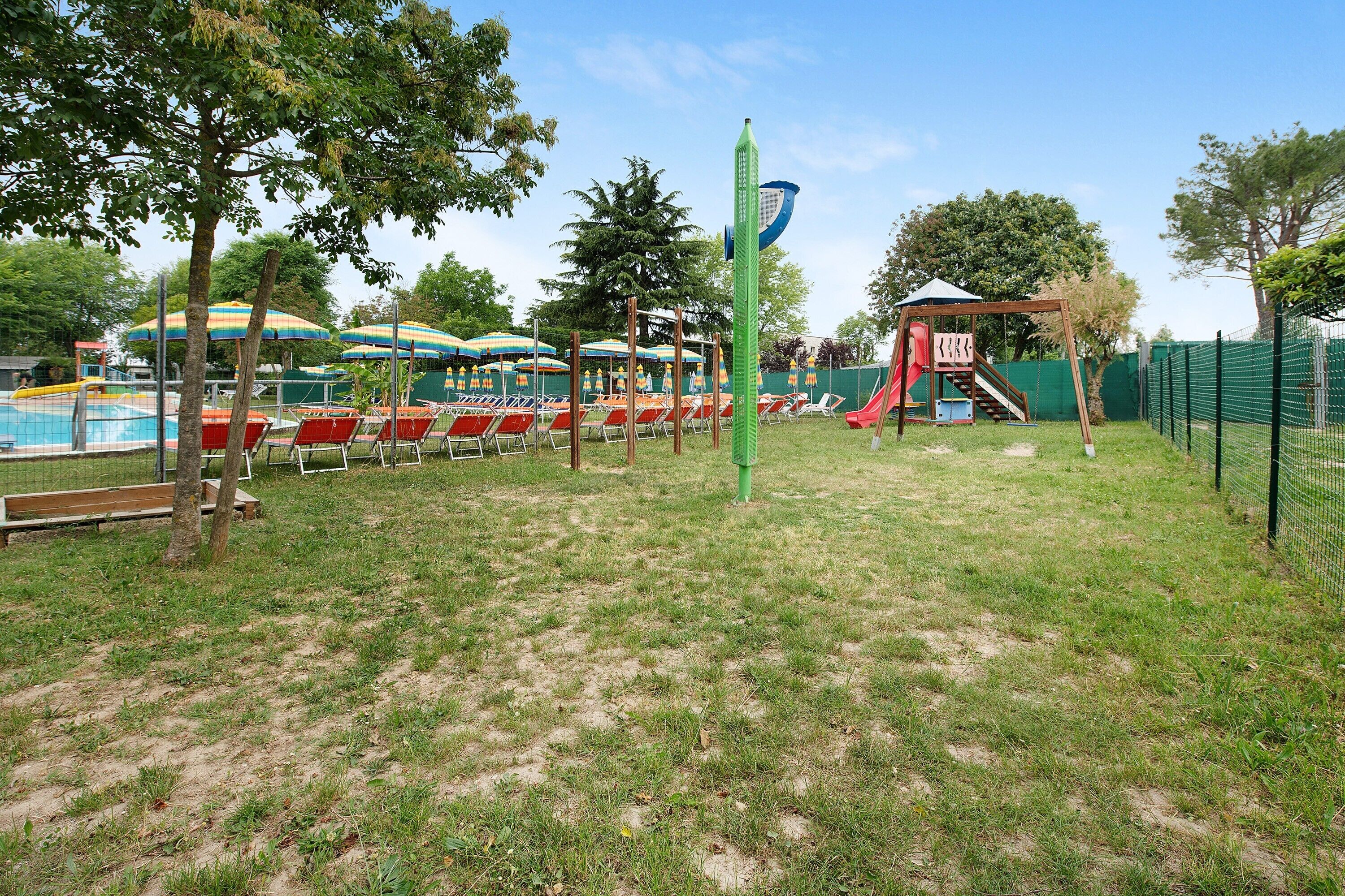 Ein Spielplatz mit Rutschen und Schaukeln, umgeben von Bäumen und Sonnenschirmen.