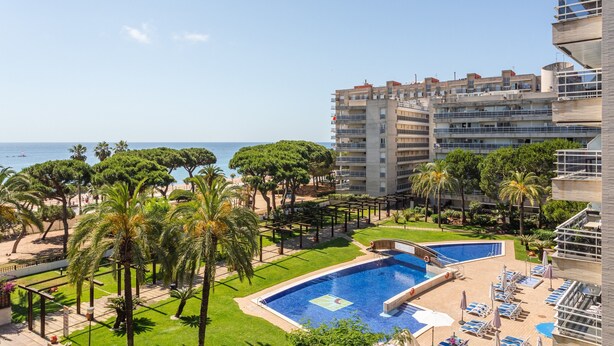 Um hotel com piscina, palmeiras e vista para o mar.