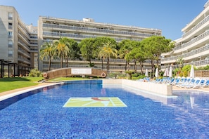 Una piscina con solárium empedrado, palmeras y un edificio de varios pisos al fondo.