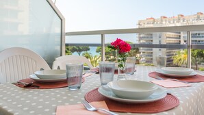 Mesa de jantar posta com pratos, copos e talheres, com vista para um edifício e vegetação.