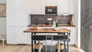 Una cocina moderna con armarios blancos, una encimera de madera, un microondas negro y una mesa de comedor con dos sillas.