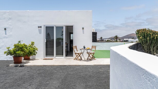 Un edificio moderno con fachada blanca, puerta de cristal de entrada y un patio con mesa y sillas.