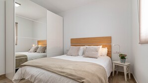 Un dormitorio con un espejo grande, un cabecero de madera, una mesita de noche con una planta y una cama con una manta color beige.