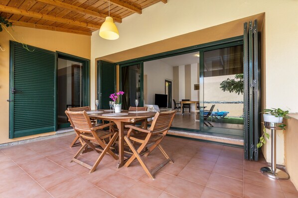 A patio with a round table and chairs, a hanging light fixture, and a sliding glass door leading to an outdoor area.