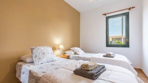 Un dormitorio con dos camas, una mesita de noche, una lámpara, una ventana con vistas y una luz en el techo.