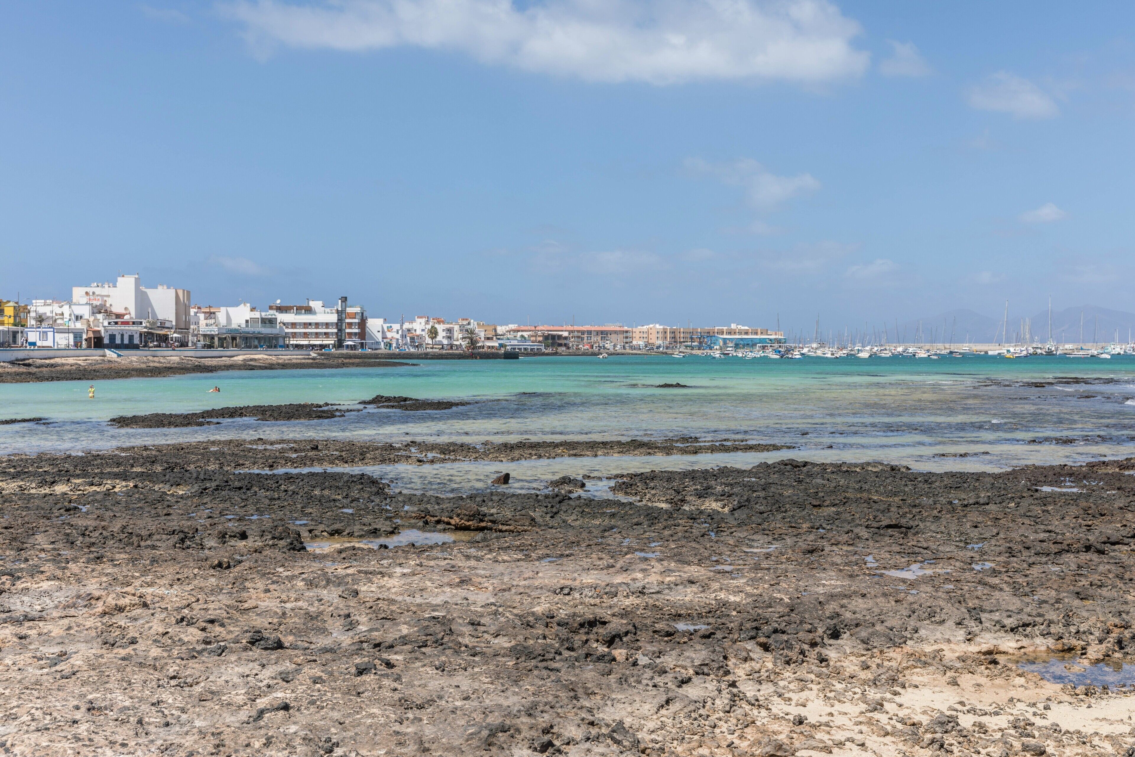 Un paisaje urbano costero con edificios, un puerto deportivo y un litoral rocoso.