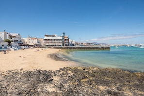 A coastal town with a sandy beach, rocky shoreline, and buildings with balconies overlooking the sea.