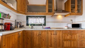Una cocina con armarios de madera, microondas, tostadora y una ventana con cortina.