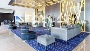 A modern lobby with a blue carpet, grey sofas, and a decorative wall with gold accents. - Staycae Celestia (Dubai)